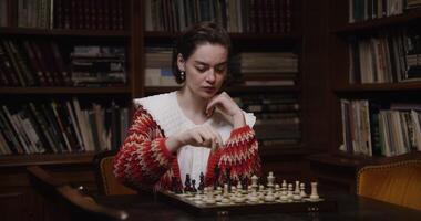A woman of European appearance plays a chess game alone, thinking long concentratedly between moves, sitting at a table in the library photo
