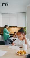 A girl draws with a stylus on a tablet while sitting at the kitchen table at home. photo