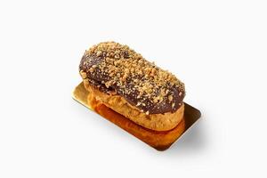 Delicious eclair covered with chocolate and peanuts resting on golden tray photo
