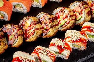 Tempura and eel sushi rolls with salmon and avocado filling resting on a black stone plate photo