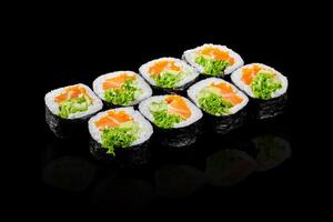 Sushi rolls with salmon, avocado, salad and fish eggs reflecting on black background photo