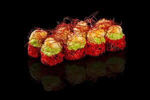 Delicious red sushi rolls topped with shrimp and guacamole with saffron reflecting on black background photo