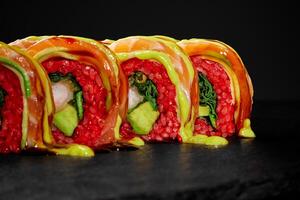 Uramaki sushi rolls with salmon, avocado, and red rice drizzled with sauce on a black background photo