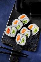 Delicious uramaki sushi rolls with salmon, cucumber, and soy sauce being served on a tray photo