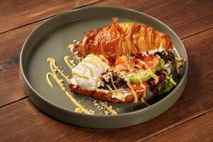 Delicious croissant sandwich with shrimps, avocado, and salad on a plate photo