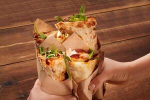 Hands holding pizza wraps with arugula on rustic wooden table photo