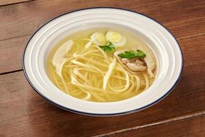 Chicken soup with noodles, quail eggs and parsley resting on wooden table photo