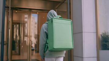 Delivery person approaches a building entrance carrying a green delivery bag in a bustling city environment photo