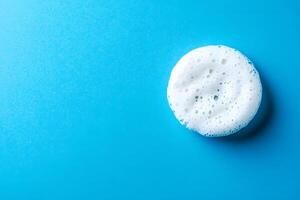 A blob of white foam rests against a vibrant blue background, creating a clean contrast photo
