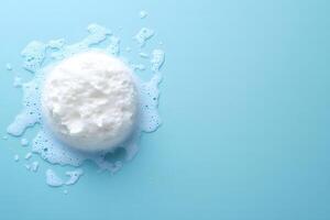 A white bath sponge sits surrounded by bubbles on a light blue background, clean and minimalist photo