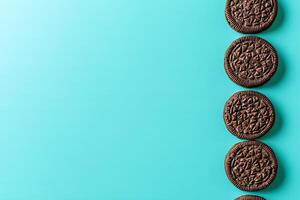 Crispy chocolate cookies with cream filling are perfectly lined on a vibrant turquoise background photo