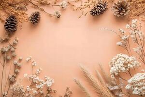 Delicate white dried flowers and assorted pinecones frame a soft, peach colored background photo