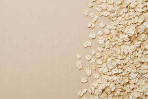 Dry rolled oats cascade across a soft beige surface, leaving a spacious blank canvas alongside them photo