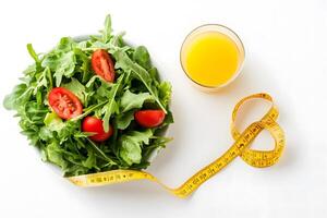 Arugula and tomatoes reside in a white bowl with orange juice and yellow tape photo