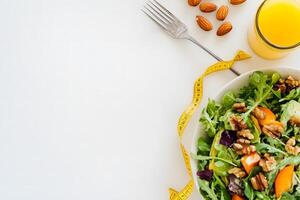 Fresh salad with walnuts and arugula, a glass of juice and almonds on white surface photo