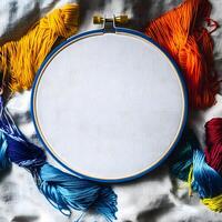Embroidery hoop encircles white canvas surrounded by vibrant threads on crumpled white fabric create an artistic composition photo