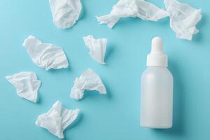 White dropper bottle stands amidst used tissues against a pastel blue background from above photo
