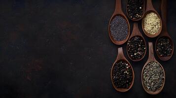 Several wooden spoons filled with an array of spices are displayed on a dark surface photo
