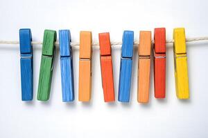 Multicolored wooden clothespins in green, blue, orange, red and yellow hang on a thin rope photo