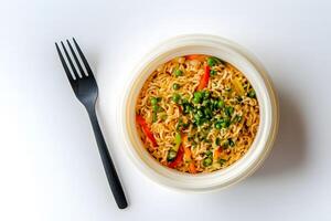 Noodles with peas and vegetables in a bowl next to a black fork on white photo