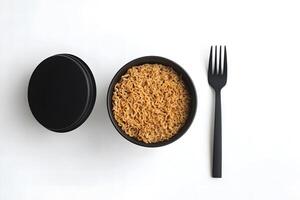 Cooked noodles served in a black bowl are alongside a black fork and lid photo