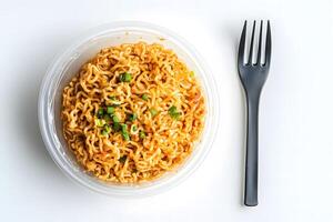 Overhead shot shows ramen noodles with scallions beside a fork on white surface photo