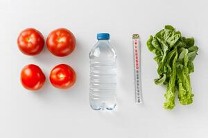 Flat lay shows tomatoes, water bottle, measuring tape, and lettuce on white background photo