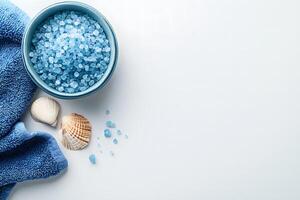 Blue bath crystals rest inside a bowl beside seashells and a blue towel photo