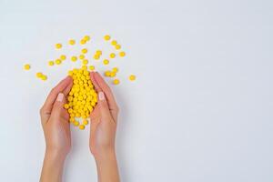 Two fair skinned hands cradle a pile of yellow round pills on white backdrop photo