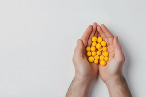 Man holds several vibrant yellow vitamin capsules in open palms against a white backdrop photo