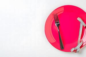 Shiny pink plate alongside a silver fork and measuring tape signify mindful eating photo
