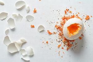 A broken white egg showcasing a vibrant yellow yolk sits among its scattered shell pieces photo
