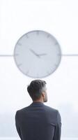 Man in formal attire gazing at large wall clock in modern office space, reflecting on time and productivity in a minimalist environment photo