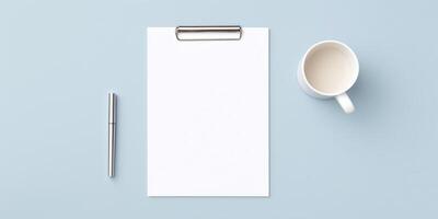 Blank clipboard with white sheet of paper, silver pen, and white coffee mug on a light blue background creating a minimalistic workspace atmosphere photo