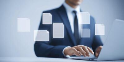 Businessman in formal attire working on laptop with floating document icons representing digital file management and organization in modern workspace photo