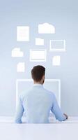 Man in blue shirt working at a computer with digital icons representing files and documents floating above in a modern workspace with copy space photo