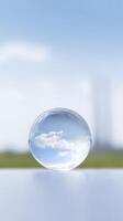 Transparent glass sphere reflecting clouds and blue sky, placed on a smooth surface with a blurred green background creating a serene atmosphere photo