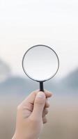 Hand holding a magnifying glass against a blurred natural background, emphasizing the concept of exploration, discovery, and observation in a serene outdoor environment photo