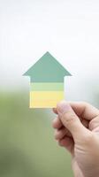 Hand holding a green and yellow arrow-shaped paper cutout against a blurred natural background, symbolizing growth, direction, and positive change in a creative and inspiring way photo
