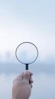 Hand holding a magnifying glass against a blurred background, emphasizing clarity and focus, symbolizing exploration and discovery in a serene environment photo