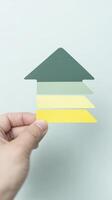 Hand holding a series of colored paper strips arranged in an upward arrow shape, symbolizing growth and progress against a soft pastel background photo