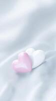 Two glossy heart-shaped objects, one pink and one white, resting on a soft, textured fabric background, symbolizing love and affection in a serene setting photo