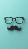 Fake mustache and eyeglasses forming a face on turquoise background photo