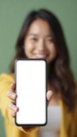Smiling woman showing smartphone with blank white screen on green background photo