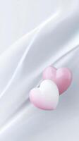 Two glossy hearts, one pink and one white, resting on a soft, flowing fabric background, creating a romantic and serene atmosphere for love-themed designs photo