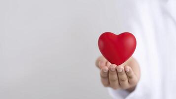 Hand holding a vibrant red heart symbol, representing love and compassion, against a soft neutral background, conveying warmth and emotional connection in a minimalist setting photo