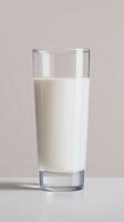 Clear glass filled with fresh milk stands on a white surface against a soft beige background, showcasing the creamy texture and inviting appearance of the beverage photo