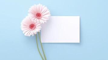 Pink gerbera daisies with green stems are positioned beside a blank white card on a soft blue background, creating a serene and inviting atmosphere for messages or notes photo