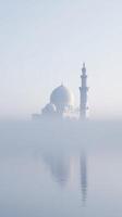 Majestic white mosque emerges from thick fog, reflecting beautifully on calm water, creating a serene atmosphere of tranquility and spirituality in a minimalist landscape photo