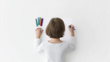 Child with short brown hair is drawing on a blank sheet of paper, surrounded by colorful markers, showcasing creativity and artistic expression in a minimalistic environment photo